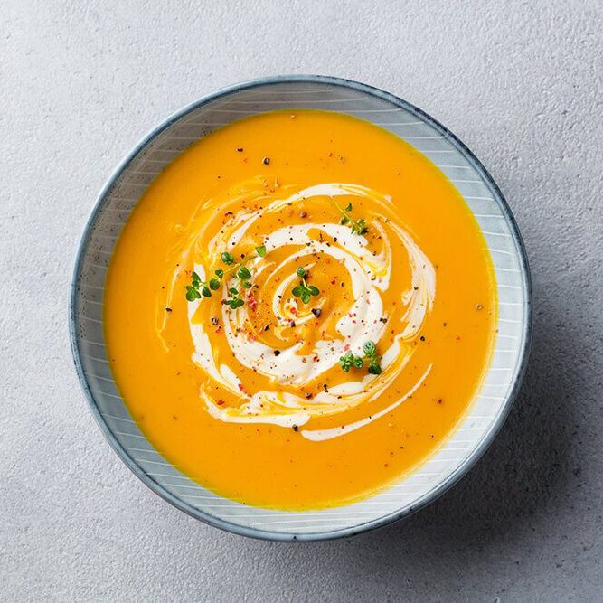 Pumpkin and carrot soup with cream on grey stone background. Close up. Top view.